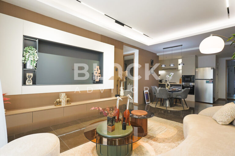 ATREUS Brookside show apartment living room with a curved sofa, a built-in TV wall and the kitchen beyond
